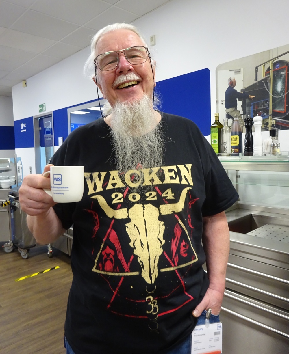 Foto von Fritz, lachend, im Wacken-T-Shirt und mit Tasse des VdS-Bildungszentrums in der Hand 