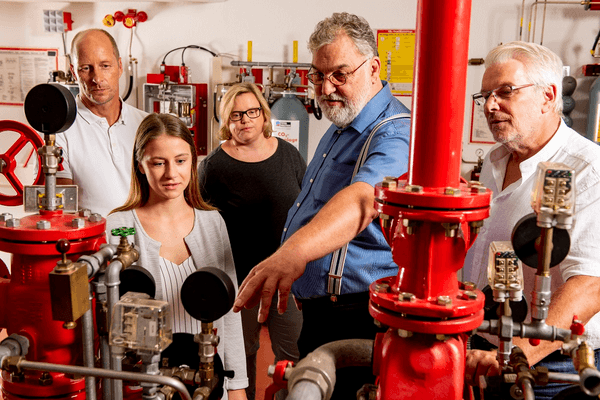 Teilnehmende besichtigen den VdS-Demobereich mit Brandschutzanlagen und roten Rohrleitungen.