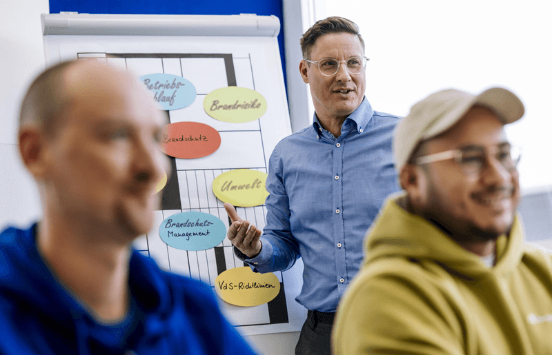 Trainer erläutert zentrale Aspekte des Brandschutzmanagements vor Flipchart mit Schlagworten wie Betriebsablauf, Brandrisiko-Management und Brandschutzprozesse – praxisnahe Fortbildung zur Optimierung innerbetrieblicher Sicherheitsprozesse.